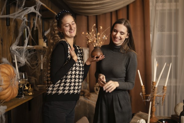 Two friends enjoy each others company as they prepare for an autumn celebration. They are decorating with handmade crafts, showcasing their creativity and joy in a warm, inviting home atmosphere