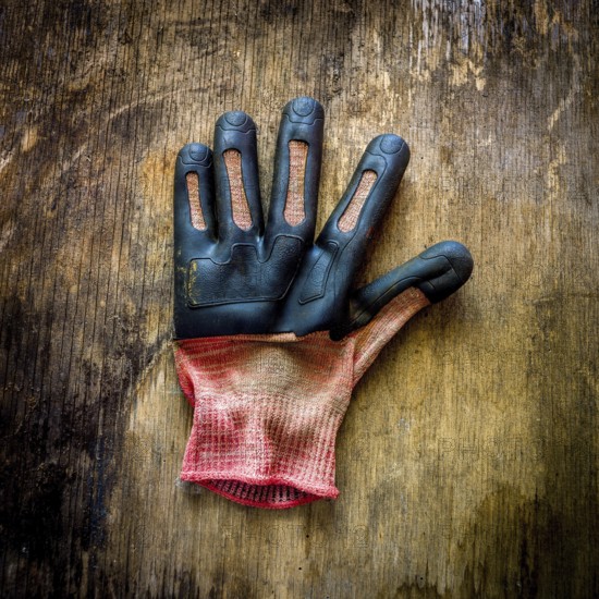 A single gardening glove lies on a rustic wooden surface, showing signs of wear and dirt from outdoor gardening activities. It reflects the hands-on nature of gardening work