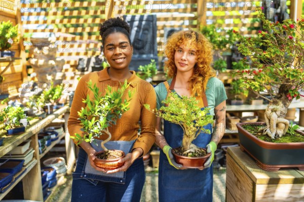 Two female gardeners holding and caring for bonsai trees while working together in a vibrant plant nursery or garden center