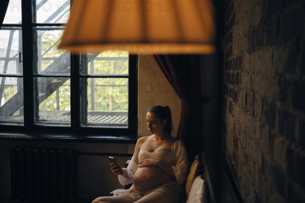 In a cozy room filled with natural light, a pregnant woman sits comfortably on sofa and making delivery order on mobile app