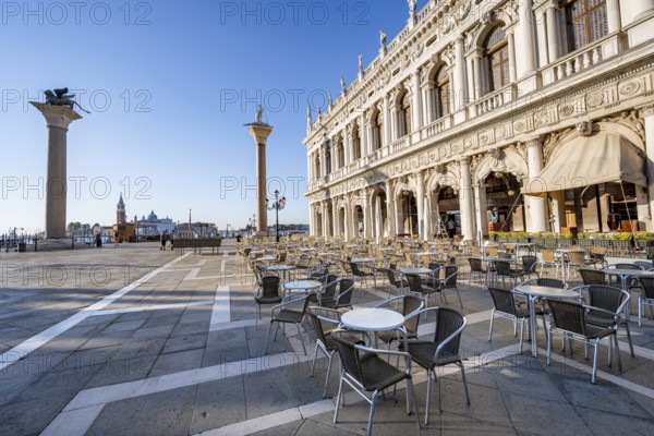 Chairs and tables of cafes at Piazetta San Marco, Colonna di San Marco and Colonna di San Todaro, in the morning light, St Mark's Square, Venice, Veneto, Italy