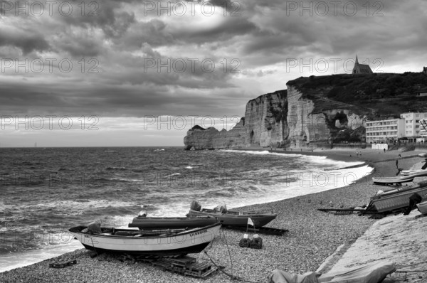 Boats lying on the beach, pebble beach, rock arch Falaise or Porte d'Amont, church Chapelle Notre Dame de la Garde, Étretat, sea, steep coast, cliffs, chalk cliffs, alabaster coast, La Côte d'Albâtre, black and white, Normandy, Seine-Maritime, France