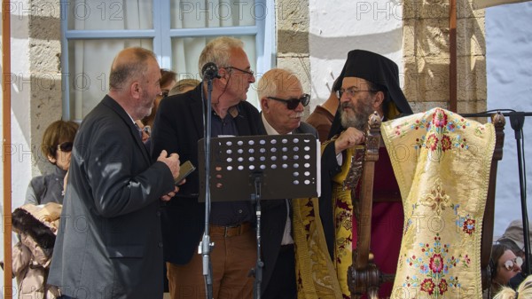 Several men, including priests, discussing in front of a crowd, one holding a microphone, surrounded by traditional clothing, Orthodox ceremony, monks of St John's Monastery, ceremonial washing of feet, procession, Maundy Thursday, Megali Pempti, Chora, Patmos, Dodecanese, Greek Islands, Greece
