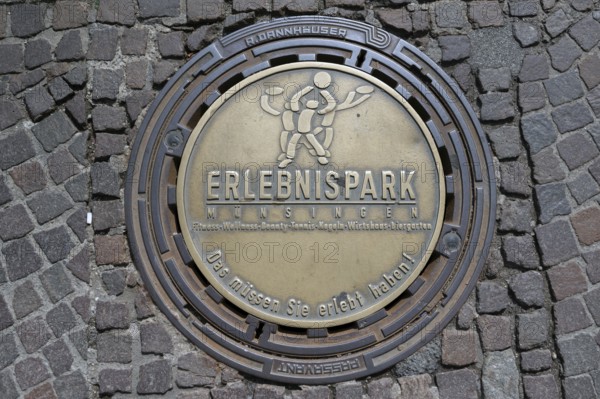 Municipal manhole cover with an advert for an adventure park, Biberach an der Riß, Baden-Württemberg, Germany