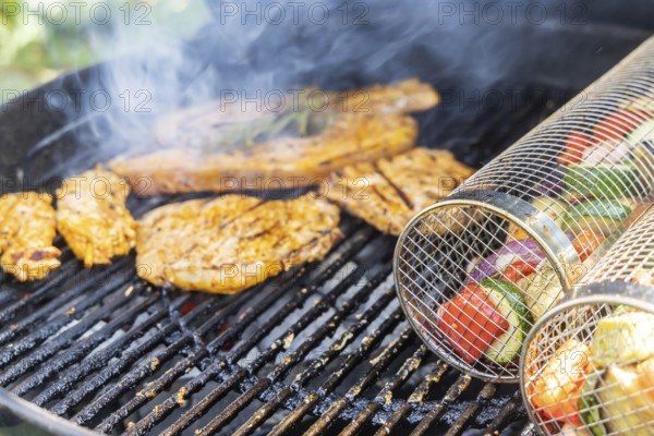 Barbecue in the garden. Meat and vegetables, vegetarian and vegan, are served on the kettle grill. Barbecue baskets for gently braising carrots, courgettes or peppers are right on trend. Münsingen, Baden-Württemberg, Germany