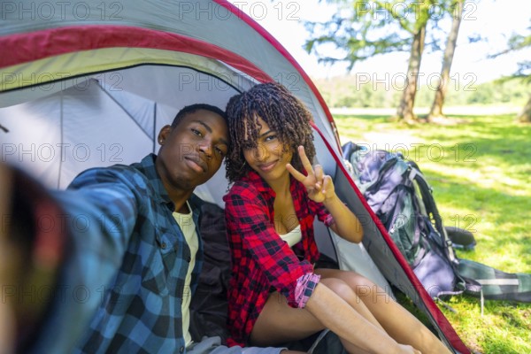 Young couple taking a selfie inside their tent while camping in nature, enjoying a relaxing vacation