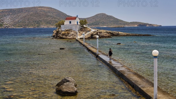 Person walking on jetty to chapel in calm blue sea under clear sky, chapel, church, Agios Isidoros, rocky islet, bay of Gourna, Kokkali, Leros, Dodecanese, Greek Islands, Greece