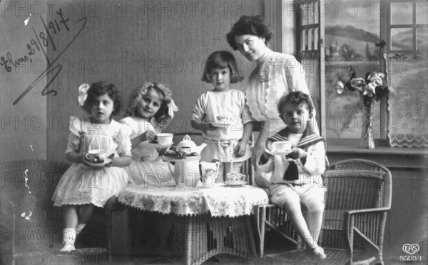 Mother with children around a coffee table, 1920s, Four children and a woman enjoying a tea party together, historical photo