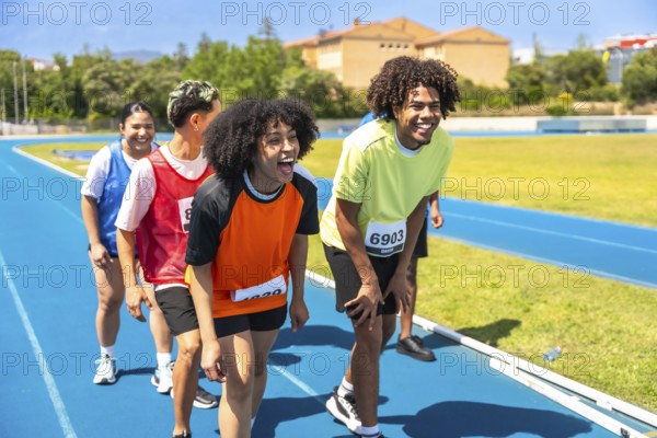 Group of athletes catching their breath and recovering after completing a race on a vibrant blue track, celebrating their achievements together