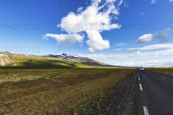 Tarmac road through barren volcanic landscape with a view of the snow-covered Snæfellsjökull volcano, Snäfellsjökull, Snaefellsjökull glacier, spring clouds, Snæfellsnes peninsula, Iceland