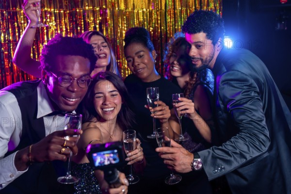 Group of cheerful multi ethnic friends taking selfie with action camera while enjoying champagne flutes at nightclub party with gold backdrop