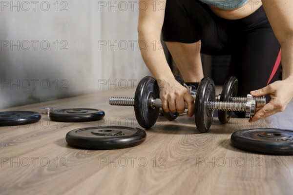 A person is adjusting weights on a dumbbell while preparing for an intense workout. The setting is a well-lit fitness center, with various weights scattered on the floor