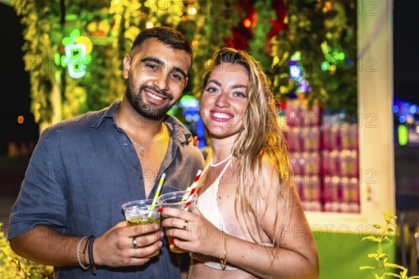 Young man and woman enjoying cocktails at a vibrant night market, celebrating summer with refreshing drinks