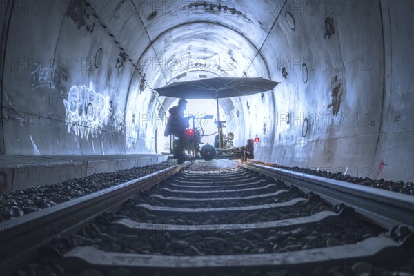 An illuminated tunnel with rails and graffiti on the walls. In the background is a figure with a large umbrella, grinding work on the Hermann Hesse railway, Ostelsheim, district of Calw, Germany