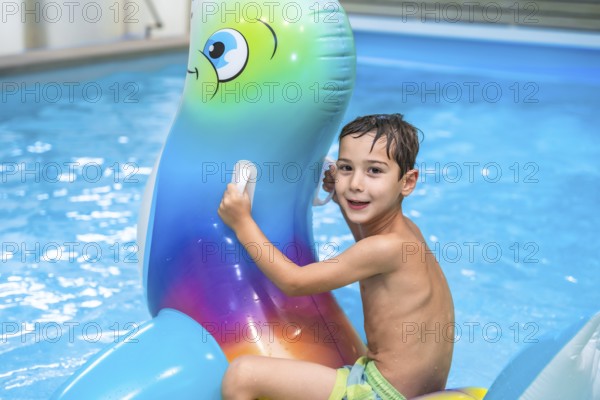 Smiling boy having fun riding an inflatable toy whale in a home swimming pool, enjoying summer vacation