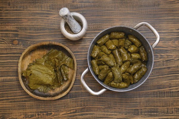 Delicious dolma is being prepared at home, featuring grape leaves wrapped around a savory filling. The cooking pot is filled with neatly arranged rolls, showcasing traditional culinary skills