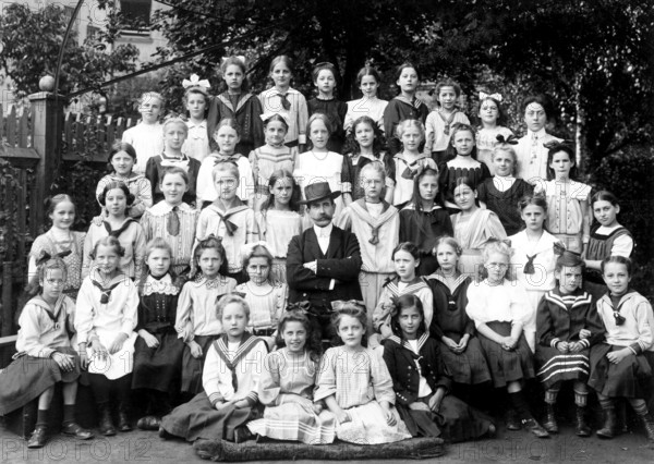 Class photo of a girl teacher, ca. 1910, group of pupils and a teacher posing together outdoors, historical photo