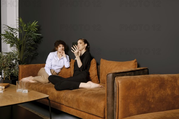 Two friends are seated comfortably on a brown couch in a modern living room. They are engrossed in a conversation while sharing smiles and laughter, creating a warm, friendly atmosphere
