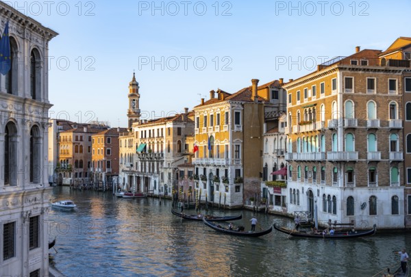 View of the Grand Canal with gondoliers at sunset, picturesque evening mood with palazzos on the canal and church tower of the Chiesa Parrocchiale dei Santi Apostoli, view from the Rialto Bridge, Venice, Veneto, Italy