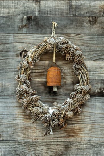 A wreath made of pinecones and natural materials is displayed on a rustic wooden wall. An antique bell adds a charming touch, Aubrac region, Occitanie.France