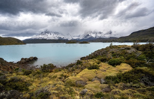 Cloudy mountain range Cuernos del Paine, shore of the blue lake Lago Pehoe in the evening light, dramatic sky, Torres del Paine National Park, Chile