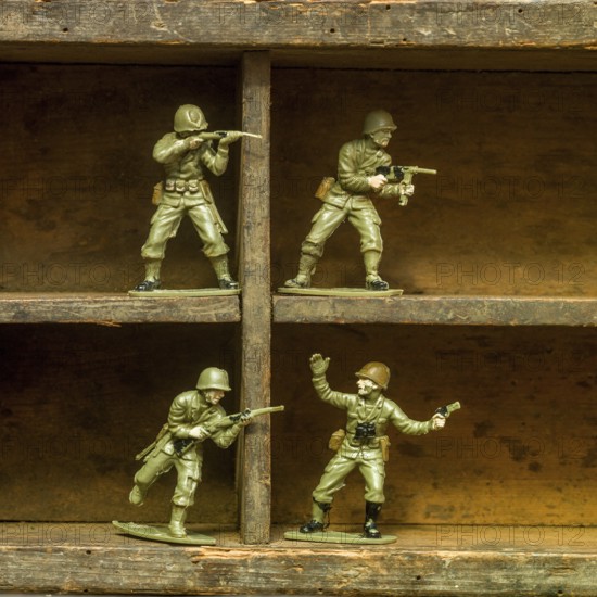 A set of classic plastic toy soldiers arranged on a wooden shelf, displaying soldiers in various action poses with rifles and gear, illustrating a playful military theme