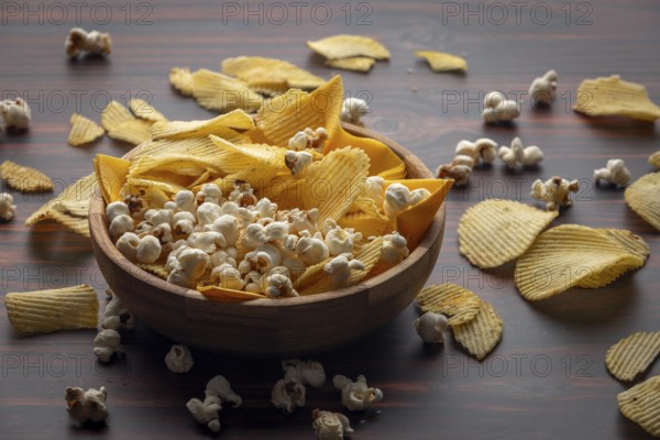 Wooden bowl with crisps and popcorn scattered on the table