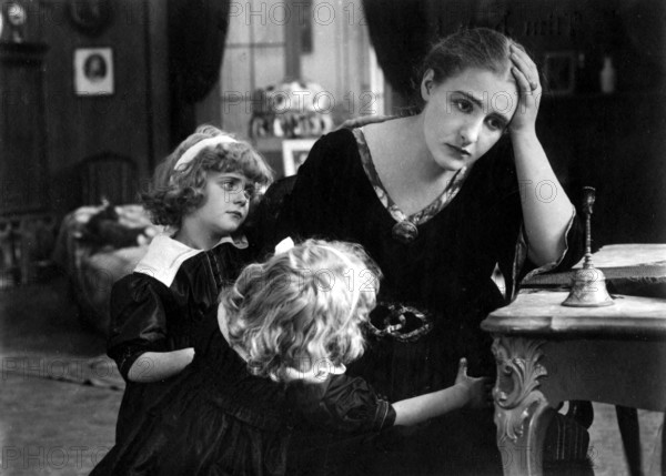 Overwhelmed mother, 1920s, A woman looks worried while two children hug her in a gloomy room, Historical photo