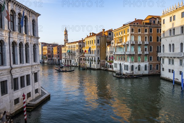 View of the Grand Canal with gondoliers at sunset, picturesque evening mood with palazzos on the canal and church tower of the Chiesa Parrocchiale dei Santi Apostoli, view from the Rialto Bridge, Venice, Veneto, Italy
