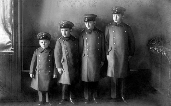 Four uniformed boys lined up in height, military, militarism, 1910s, group of boys in uniforms and caps, posing in front of a neutral backdrop, serious facial expression, historical photo