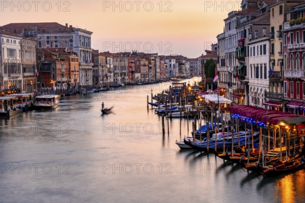 View of the Grand Canal with gondoliers at sunset, picturesque evening mood with illuminated palazzos on the canal, long exposure, view from the Rialto Bridge, Venice, Veneto, Italy