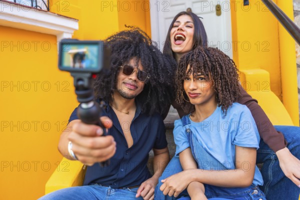 Three latin friends filming a vlog using a gimbal and action camera, enjoying laughter and smiles while sitting on vibrant yellow steps