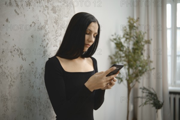 Woman with long black hair using smartphone in a minimalist indoor space during the day