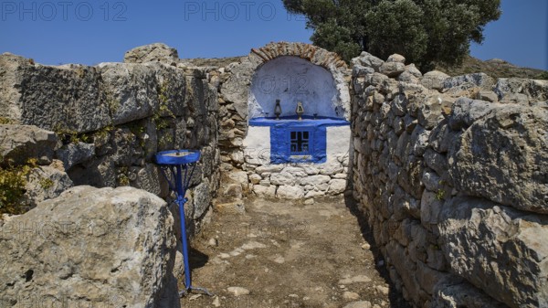 Small stone chapel with blue façade embedded in ancient ruins under a bright blue sky, Artemis Temple, Artemis, Diana, goddess of the hunt, altar. Church, tower, near the airport in the north of the island, Leros, Dodecanese, Greek Islands, Greece