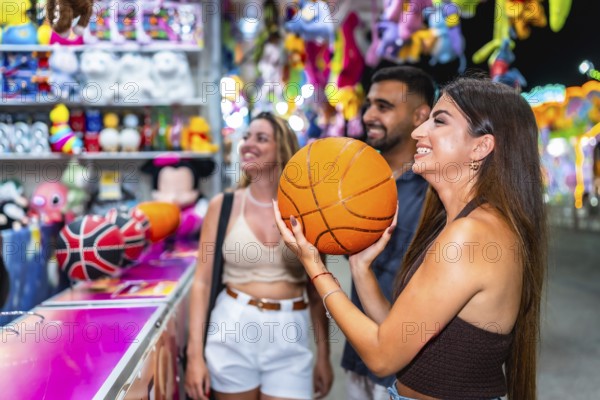 Group of friends enjoying a lively evening at a funfair game stall, celebrating their basketball win with laughter and smiles