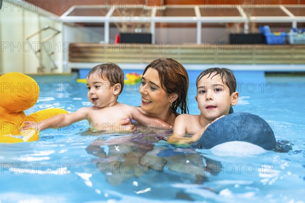 Smiling mother enjoying time with her sons while swimming in an indoor pool, playing joyfully with colorful inflatable toys