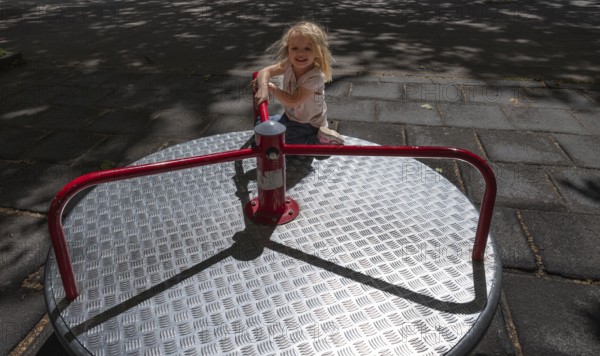 Outdoor shot, little girl, 3 years old, blonde, playing on a merry-go-round, children's playground, playground, Stuttgart, Baden-Württemberg, Germany