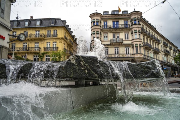 City fountain with running water in front of historic buildings on a cloudy day, Baden Baden, Germany