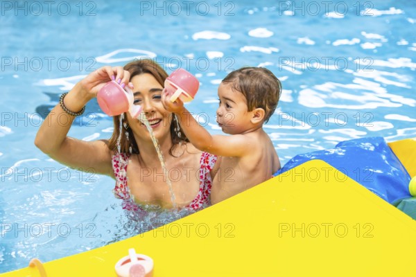 Mother and son enjoying playtime together, pouring water from pink toys in a bright yellow inflatable boat, creating a cheerful summer scene
