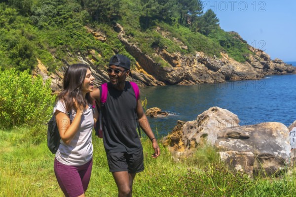 Young couple walking and laughing along a beautiful coastline path on a sunny summer day, enjoying the scenic views