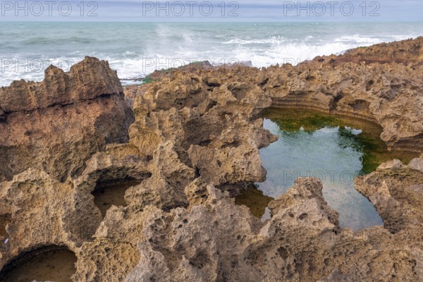 A rocky area with a hole in the ground. The hole is filled with water. The water is brown in colour. Rabat, Morocco