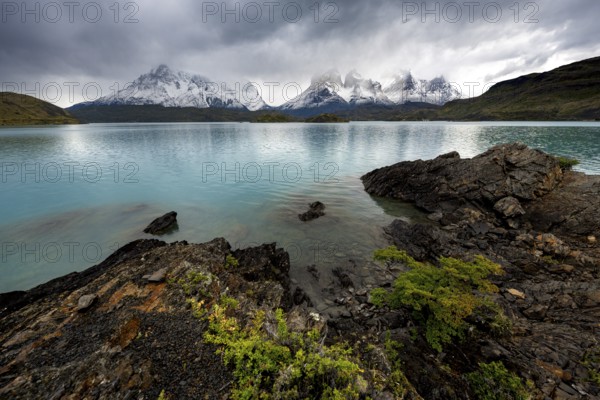 Cloudy mountain range Cuernos del Paine, shore of the blue lake Lago Pehoe in the evening light, dramatic sky, Torres del Paine National Park, Chile