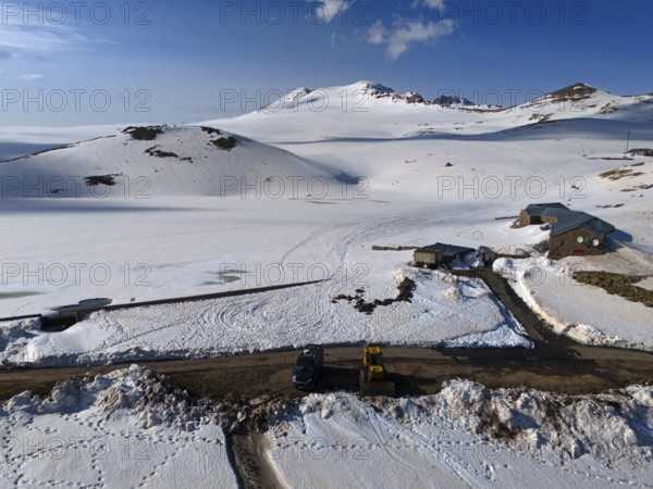 Huts and a road embedded in snow-covered mountains under a clear blue sky, aerial view, Aragaz, Aragac, Alagyaz, extinct stratovolcano, 4090 m, Aragazotn, Shirak, Armenia