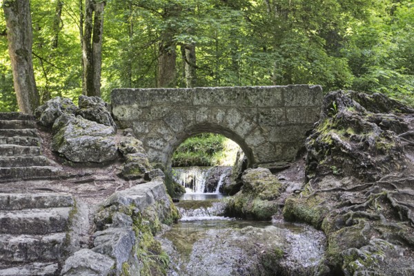 An old, small stone bridge over the Brühlbach, wild and romantic stream and source of the Urach waterfall in a dense forest, Bad Urach