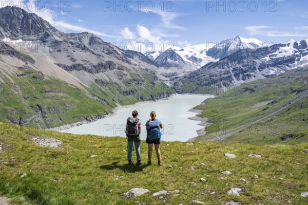 Two female friends in the mountains, mountaineers in front of a blue mountain lake, reservoir Lac des Dix, in the background mountain peak Mont Blanc de Cheilon with glacier, Hérménence, Valais Alps, Valais, Switzerland