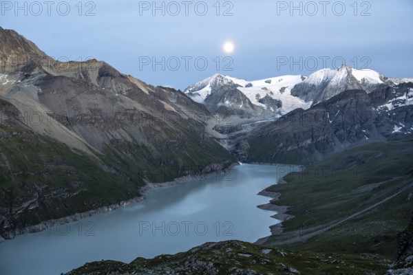 Mountain landscape with turquoise blue reservoir Lac des Dix and summit Mont Blanc de Cheilon, evening mood, moon stands above mountain peaks at the blue hour, Hérménence, Valais Alps, Valais, Switzerland