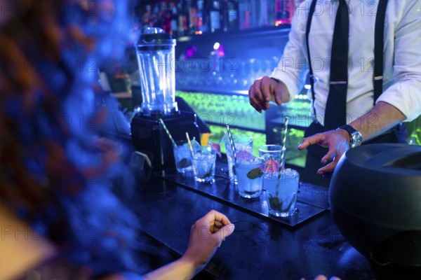 Bartender skillfully preparing vibrant blue cocktails garnished with fresh mint and ice in a lively nightclub atmosphere