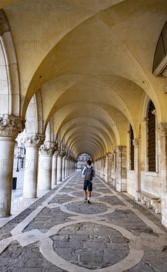 Young man walking through the portico of the Doge's Palace, St Mark's Square, Venice, Veneto, Italy