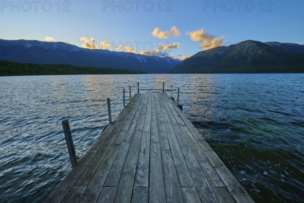 Wooden footbridge leading into a lake with mountains in the background at sunrise, summer, Lake Rotoiti, Saint Arnaud, Tasman Region, South Island, New Zealand