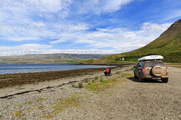 Tourist enjoying solitude in fjord landscape, SUV with roof tent, Skápadalur valley, coastline, Cirrus, Patreksfjördur, Vestfirðir, Westfjords, Iceland